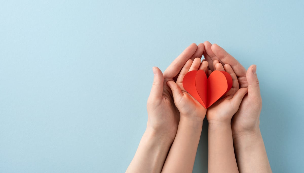 Adult and child hands holding a red heart, representing love, care, and family bonds